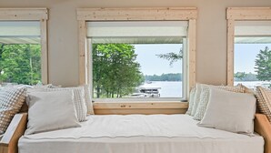 A bed with a view of a lake and dock, wooden window frames, and a view of trees. - Sand Bar Resort – Updated 5BR with Lake Views,  Big Yard, Firepit, Pontoon rental,  Gourmet Kitchen & More! (Suring)