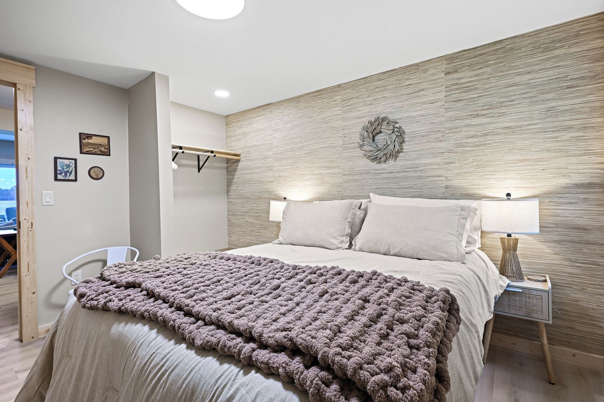 Un dormitorio ordenado con cama, lámparas de noche y estante en la pared.