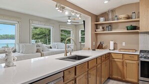 A modern kitchen with a large island, wooden cabinets, and a view of the outdoors. - Sand Bar Resort – Updated 5BR with Lake Views,  Big Yard, Firepit, Pontoon rental,  Gourmet Kitchen & More! (Suring)