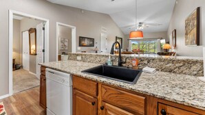 A kitchen with granite countertops, a black sink, wooden cabinets, and a ceiling fan.