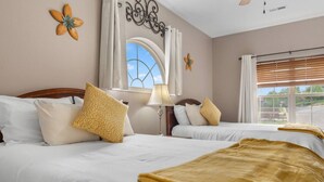 A hotel room with two beds, a window with curtains, a decorative wall piece, and a lamp.