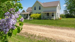 A two-story house with a porch, a lawn, and a dirt path leading to the house. - Peaceful Pepin Farmhouse Getaway (Pepin)