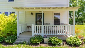 A white house with a covered porch, a small table, and potted plants. - Peaceful Pepin Farmhouse Getaway (Pepin)