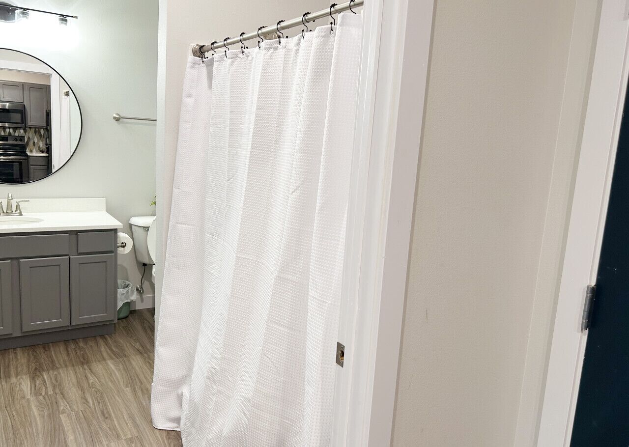 A bathroom with a shower curtain, a toilet, a sink with a mirror, and a cabinet.