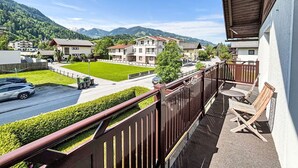 Un balcón con vista a una calle residencial, un césped verde y montañas al fondo.