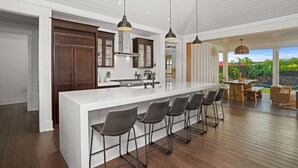 A modern kitchen with a large island, bar stools, pendant lights, and a view of the outdoors.