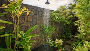 A tropical garden with a stone wall, a curved showerhead, and various plants.