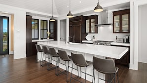 A modern kitchen with a large island, bar stools, dark wooden cabinets, and pendant lighting.