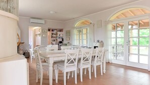 A dining area with a white table and chairs, a bookshelf, and large windows with arched tops. - Wonderful private villa for 6 guests with A/C, WIFI, TV, patio, pets allowed and panoramic view (Roccastrada)