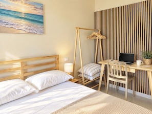 A bedroom with a bed, a desk with a laptop, a chair, and a hanging lamp.