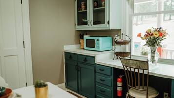 A kitchen with teal cabinets, a microwave, a chair, a fire extinguisher, and a window with flowers.