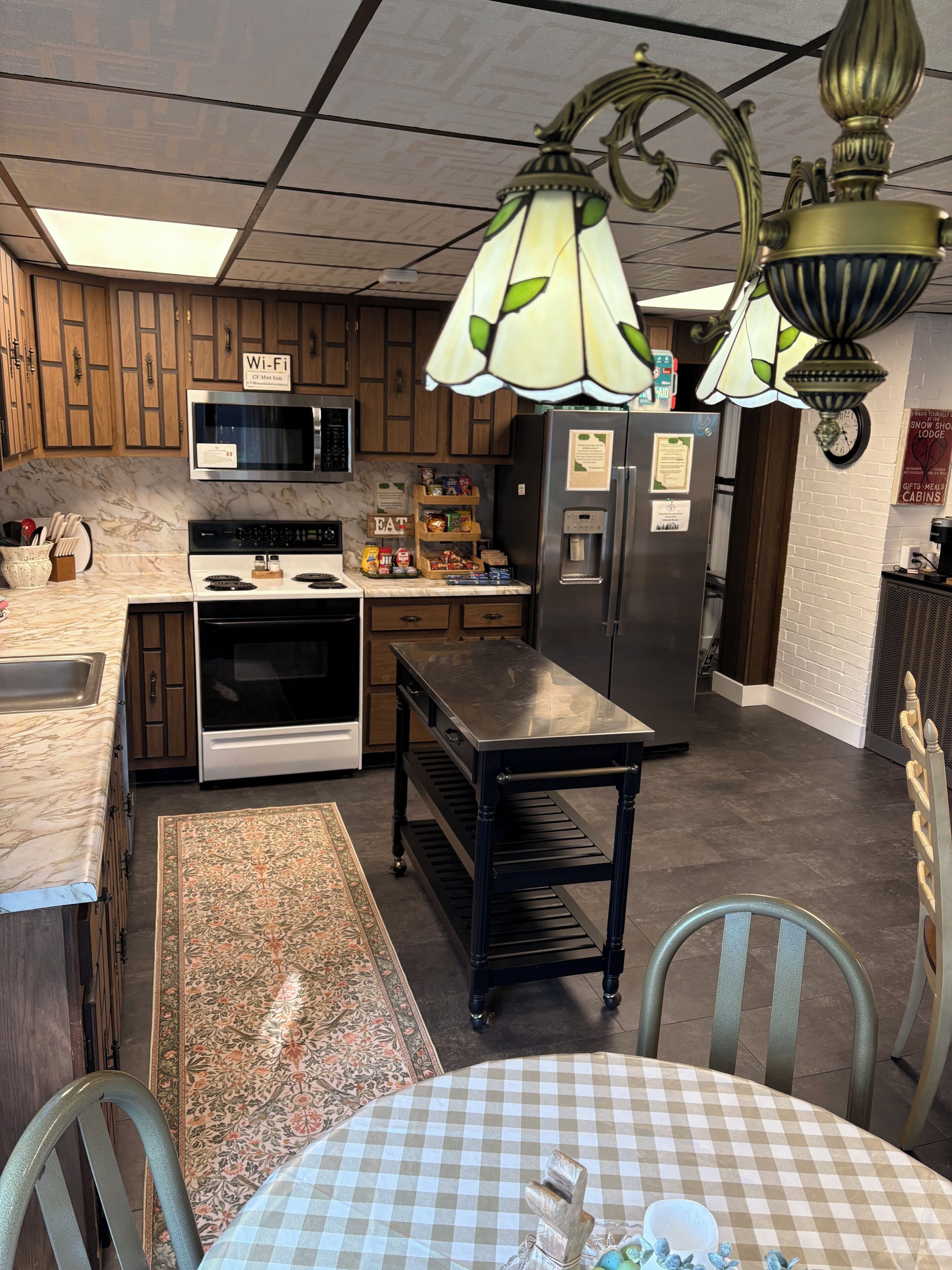 A kitchen with wooden cabinets, a microwave, stove, refrigerator, and a chandelier.