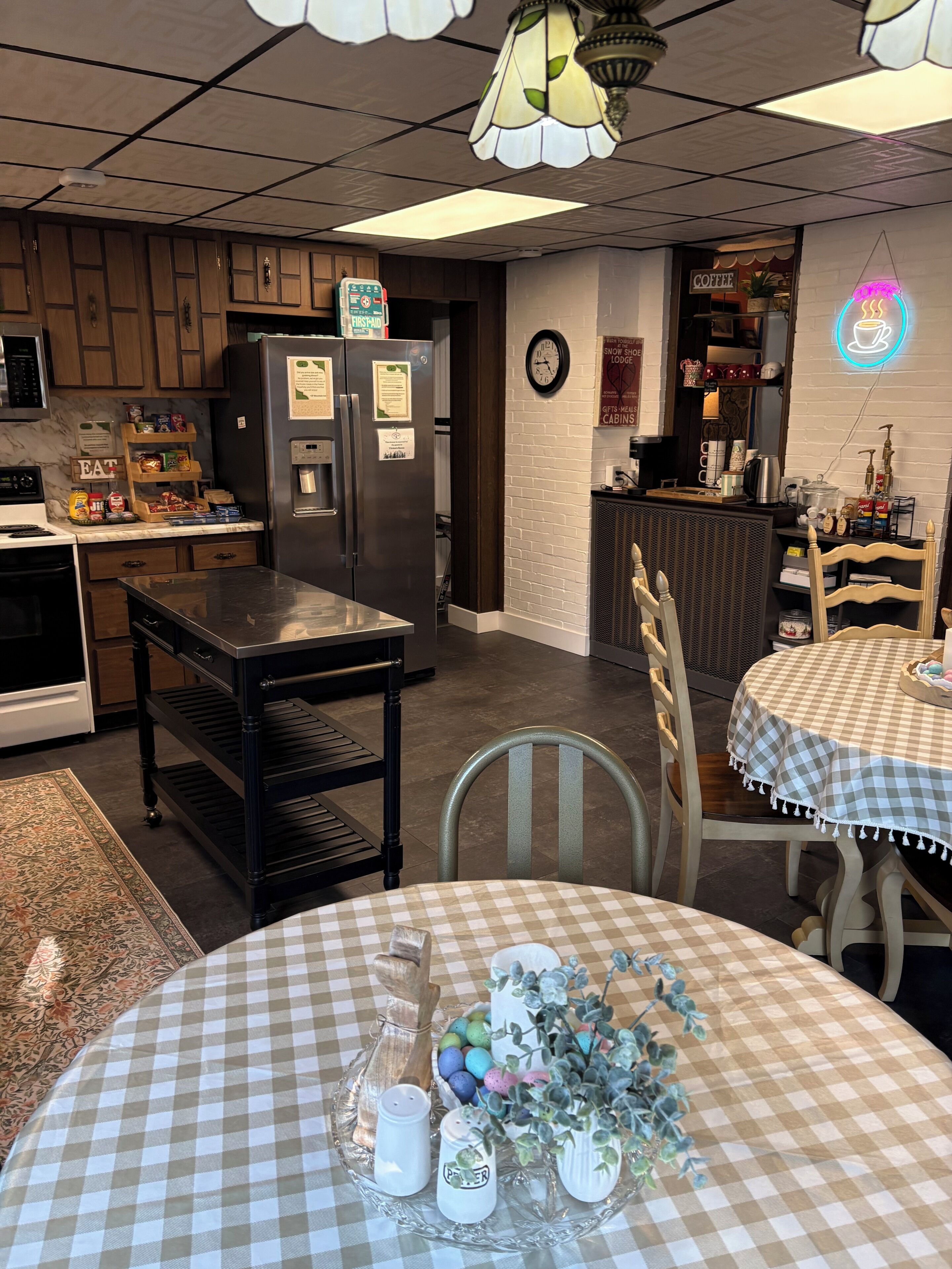 A kitchen with a refrigerator, stove, and wooden cabinets. There is a table with a checkered tablecloth and salt and pepper shakers.
