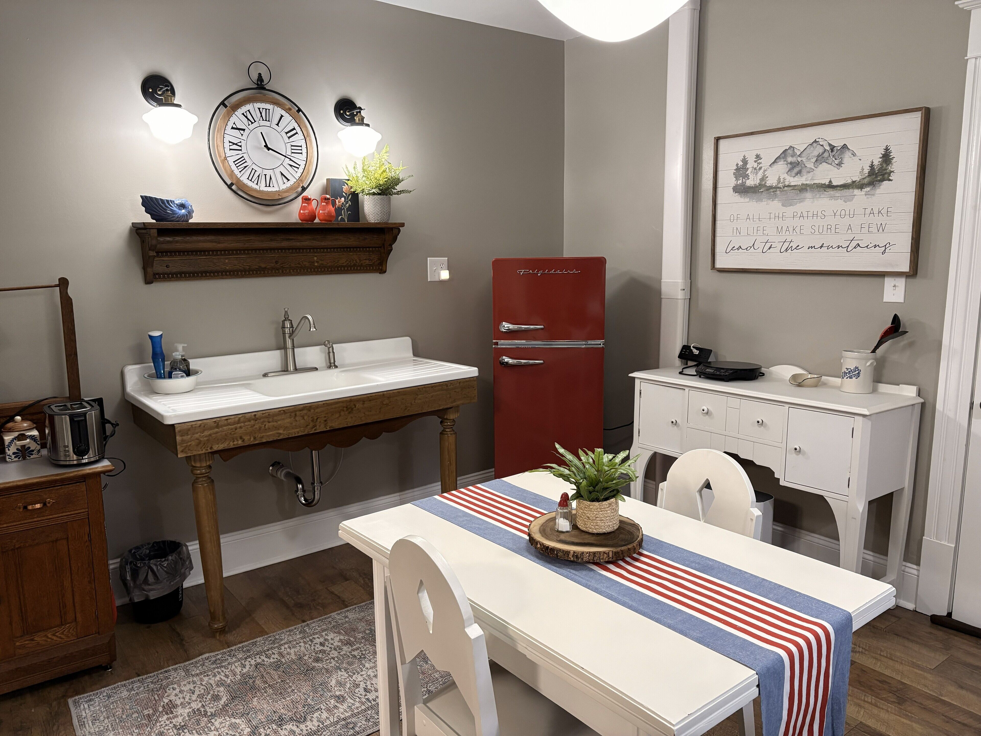 A kitchen with a wooden table, a red refrigerator, a sink, and a clock on the wall.