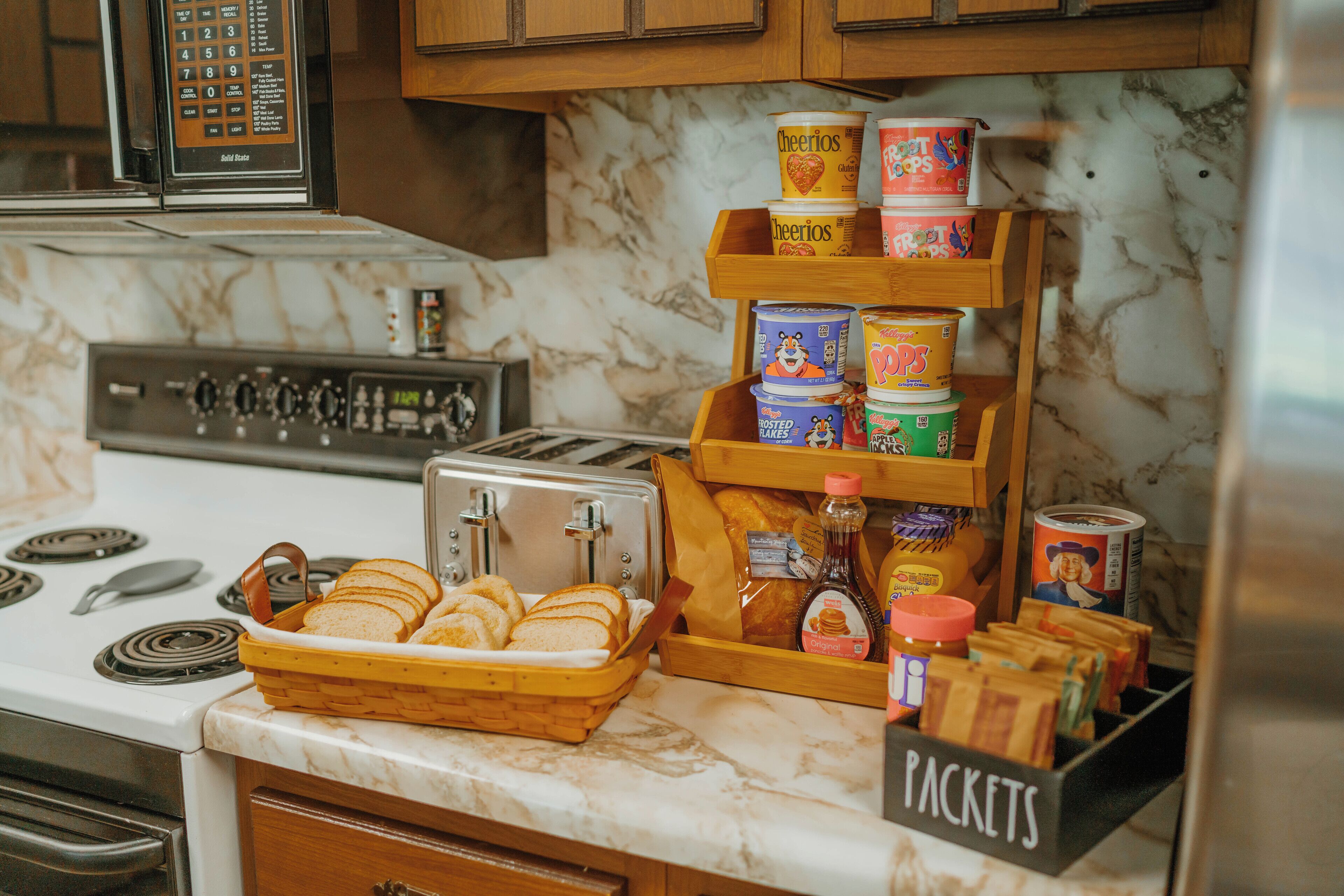 A kitchen with a marble countertop, a toaster, a bread basket, and a display of breakfast items including cereals and spreads.