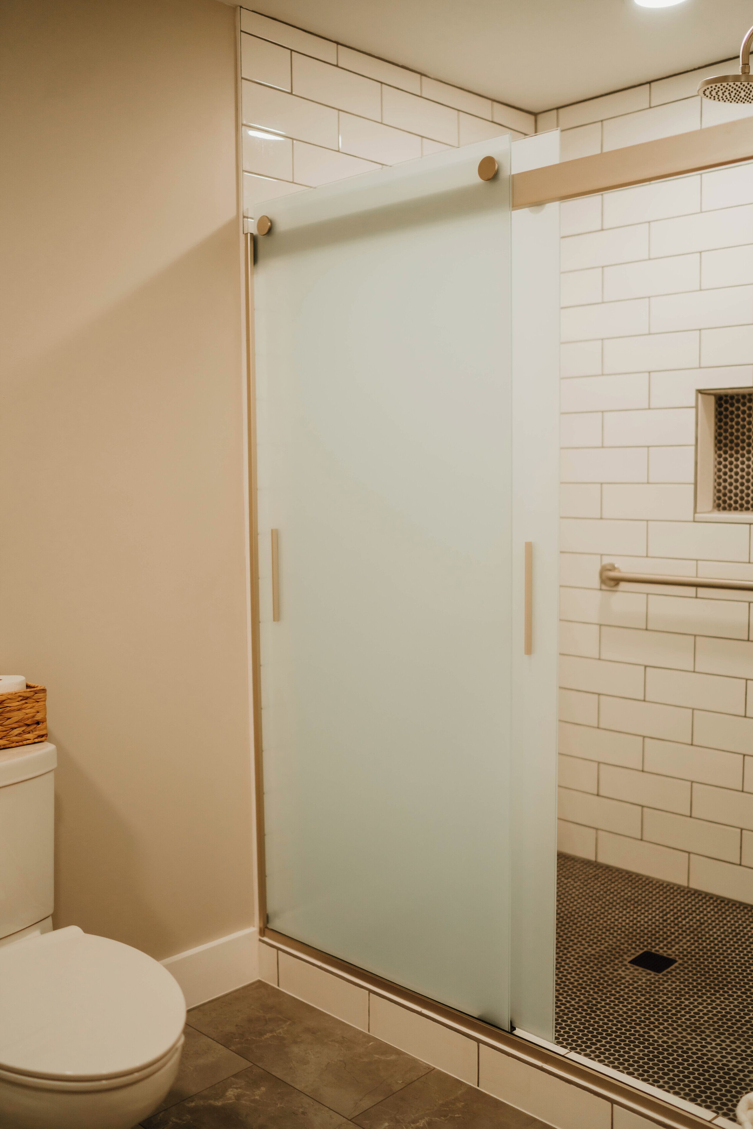 Une salle de bain avec des toilettes, une douche en verre et des murs recouverts de carrelage blanc.