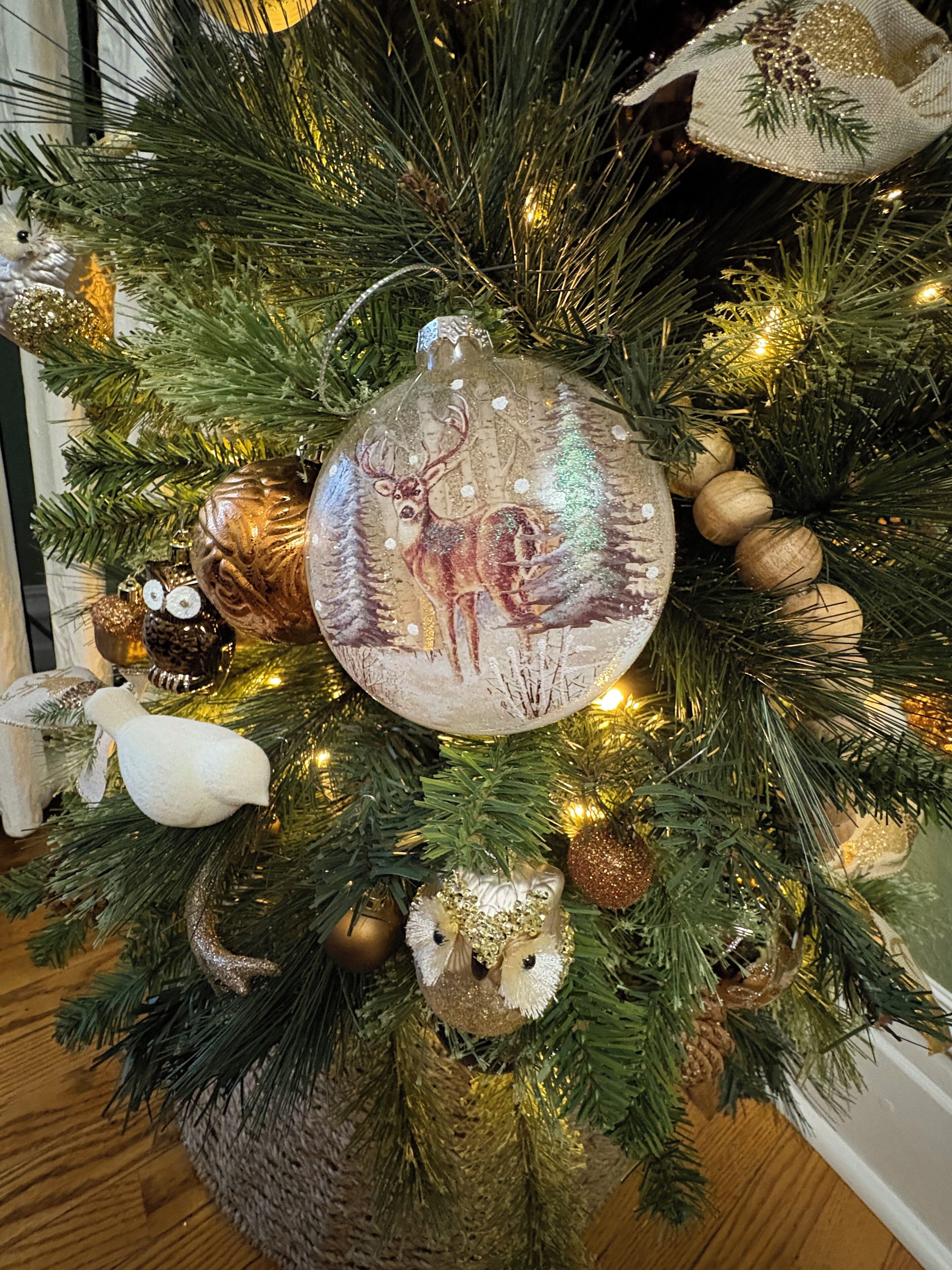 Un árbol de Navidad decorado con varios adornos, entre ellos un ciervo, un pájaro blanco y un adorno dorado.