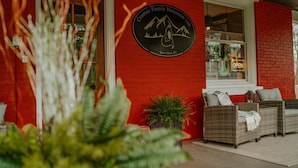 Η εξωτερική όψη του ορεινού ξενοδοχείου Cramer Family Mountain Inn, με τοίχους από κόκκινο τούβλο, μια επιγραφή, έπιπλα από μπαμπού και γλάστρες με φυτά.