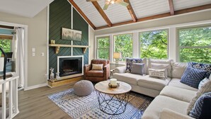 Un salon chaleureux avec une cheminée, des sièges confortables et de grandes fenêtres donnant sur un paysage verdoyant.