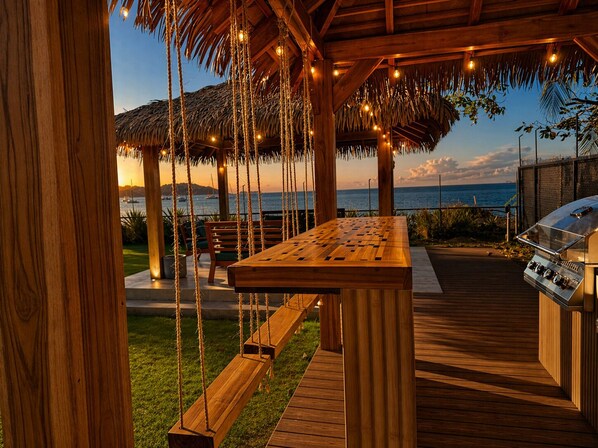 A wooden deck with a grill, a swing set, and a view of the ocean.