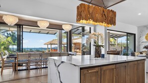 A modern kitchen with a marble island, wooden cabinets, and a view of the ocean. - Luxury Beachfront Estate w/ Private Chef, Full Staff/Concierge Resort Amenities (Playa Flamingo)