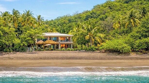 A beachfront property with a two-story house, surrounded by lush greenery and palm trees. - Luxury Beachfront Estate w/ Private Chef, Full Staff/Concierge Resort Amenities (Playa Flamingo)