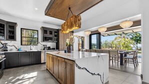 A modern kitchen with a marble island, dark cabinets, and a wooden ceiling. - Luxury Beachfront Estate w/ Private Chef, Full Staff/Concierge Resort Amenities (Playa Flamingo)