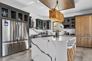A modern kitchen with a central island, stainless steel appliances, and a unique wooden pendant light.
