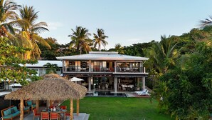 A two-story house with a pool, outdoor seating, and lush tropical surroundings. - Luxury Beachfront Estate w/ Private Chef, Full Staff/Concierge Resort Amenities (Playa Flamingo)