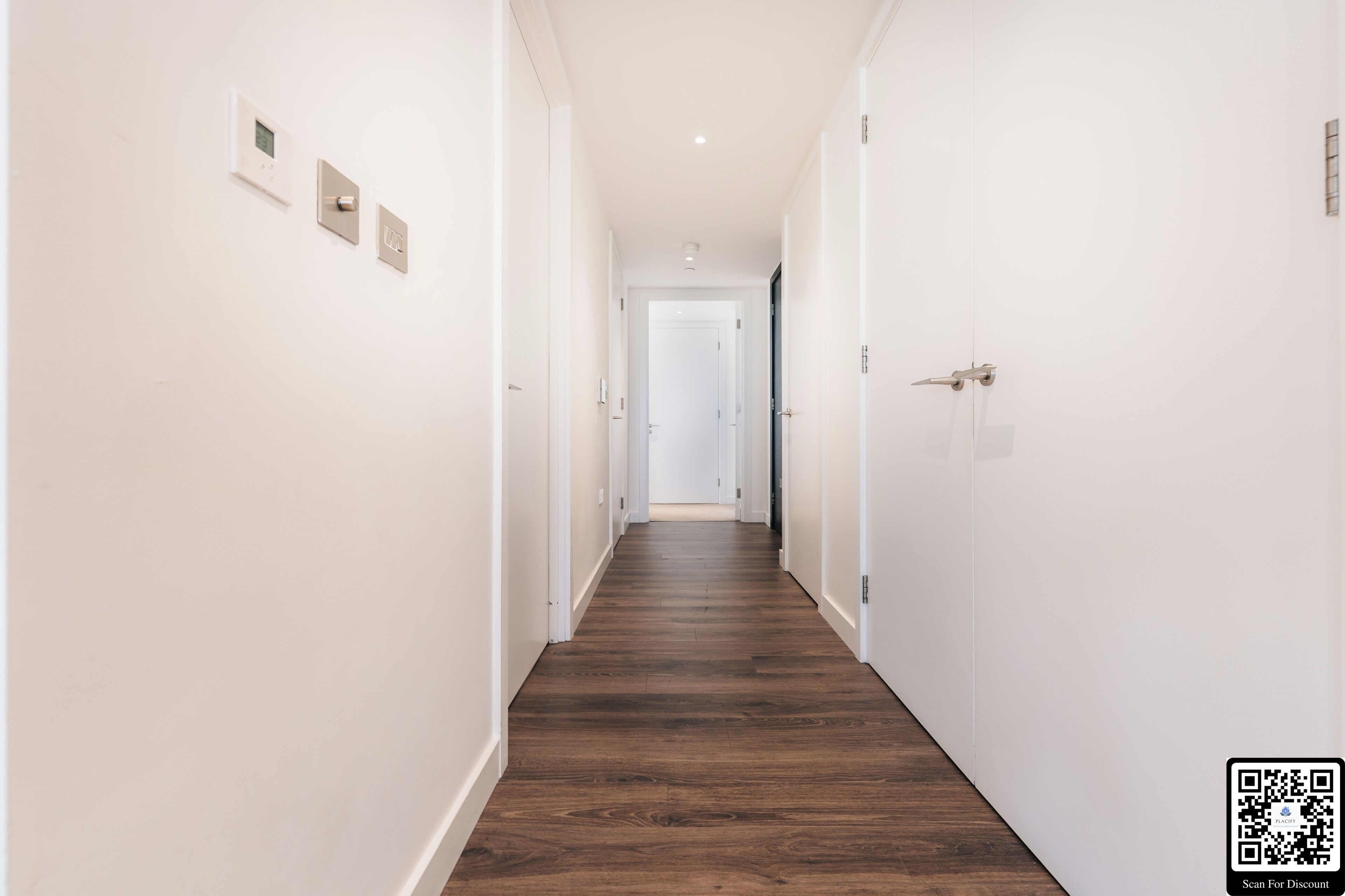 A narrow hallway with white walls and wooden flooring.