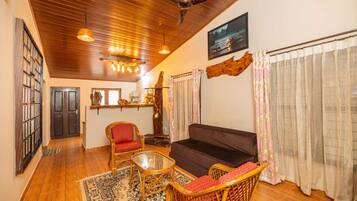A cozy living room with a dark sofa, wicker chairs, a glass coffee table, and a wooden ceiling.