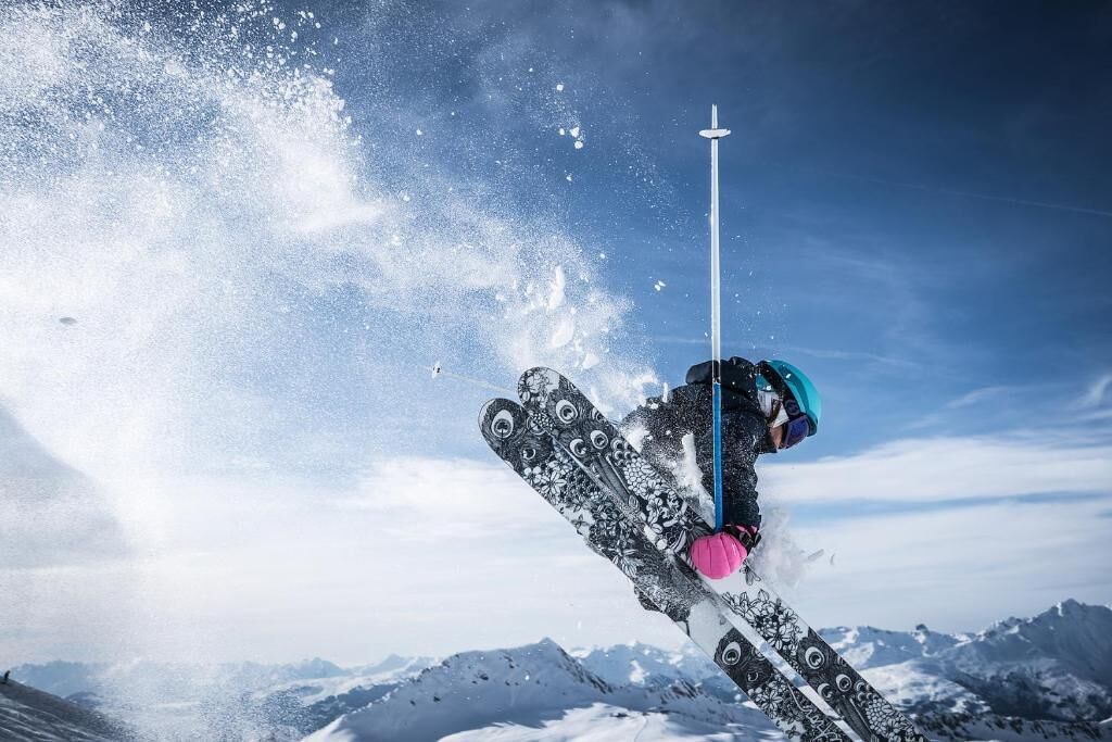 Un skieur en plein saut, en l’air, avec une montagne en arrière-plan.