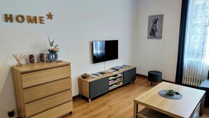 Una sala moderna con un aparador de madera, un televisor sobre un mueble bajo, una estantería y una mesa de comedor.