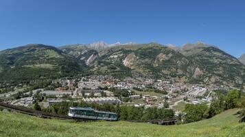 A town nestled in a valley with mountains in the background, a train on tracks, and a modern building with a glass facade.