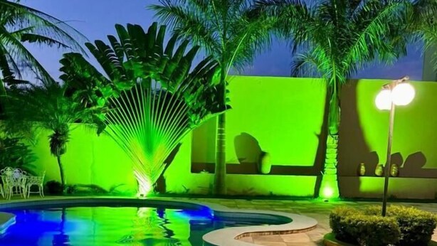 A swimming pool with a fountain, surrounded by palm trees and a green-lit wall. - Casa com Piscina - Quartos Privativos (Sao Raimundo Nonato)