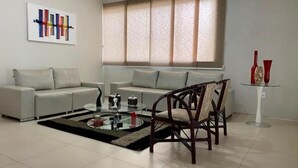 A modern living room with a sofa, a glass coffee table, and a wooden chair. - Casa com Piscina - Quartos Privativos (Sao Raimundo Nonato)