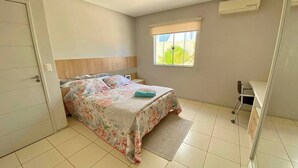 A bedroom with a bed, a bedside table, a window with a view, and a desk with a chair. - Casa com Piscina - Quartos Privativos (Sao Raimundo Nonato)