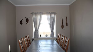A dining room with a long table, wooden chairs, a window with sheer curtains, and wall-mounted cutlery.