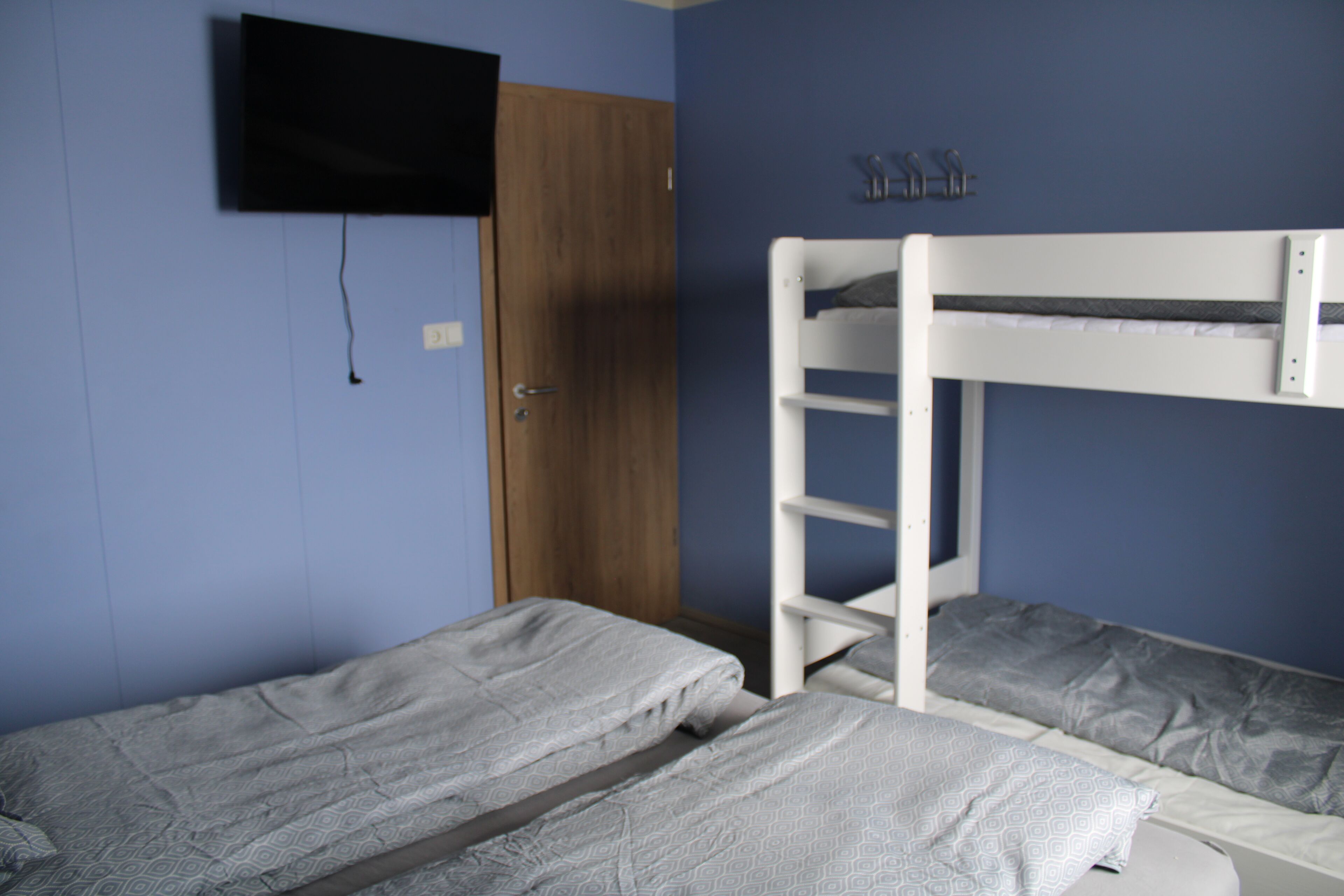 Una habitación con dos literas, una puerta de madera y un televisor montado.