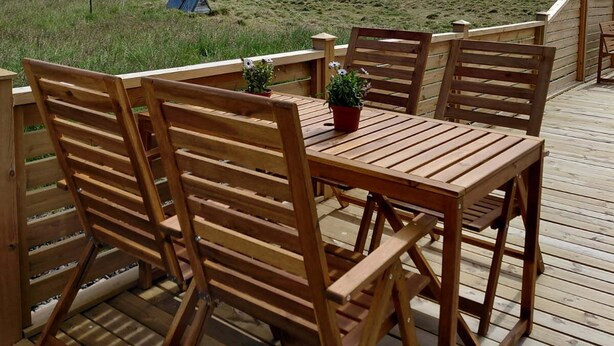 A wooden deck with a table and chairs, overlooking a grassy field with horses and a tent.