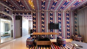 A room with a patterned ceiling, a wooden table, and a TV mounted on the wall.