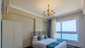 A bedroom with a bed, a chandelier, a wardrobe, and a large window with a view.