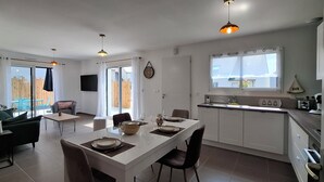 Une cuisine moderne avec des meubles blancs, un coin repas doté d’une table blanche et une grande fenêtre agrémentée de rideaux.
