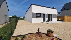 Une maison moderne à deux étages, avec une allée en gravier, une clôture en bois et un jardin agrémenté de plantes et de paillis.