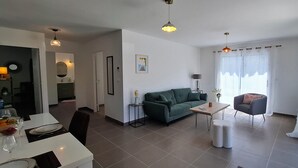 Un salon moderne avec un canapé vert, une table basse en bois et un coin repas comprenant une table et des chaises blanches.