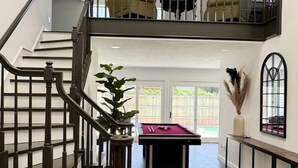 A spacious living area with a wooden floor, a pool table, and a staircase with a railing. - LUX Lounge | 3200+ SQ FT - Heated Pool & Jacuzzi (Richardson)