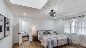 A bedroom with a large bed, a ceiling light, a bedside table, and a window with curtains. - LUX Lounge | 3200+ SQ FT - Heated Pool & Jacuzzi (Richardson)