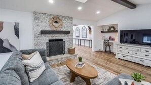 A modern living room with a fireplace, a sofa, a coffee table, and a TV. - LUX Lounge | 3200+ SQ FT - Heated Pool & Jacuzzi (Richardson)