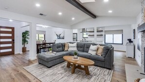 A spacious living room with a grey sectional sofa, a wooden coffee table, and a dining area with a dark wooden table and chairs. - LUX Lounge | 3200+ SQ FT - Heated Pool & Jacuzzi (Richardson)