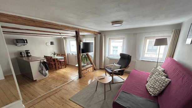 Un ambiente compatto con pavimento in legno, un divano, una TV, un'area pranzo e una cucina.